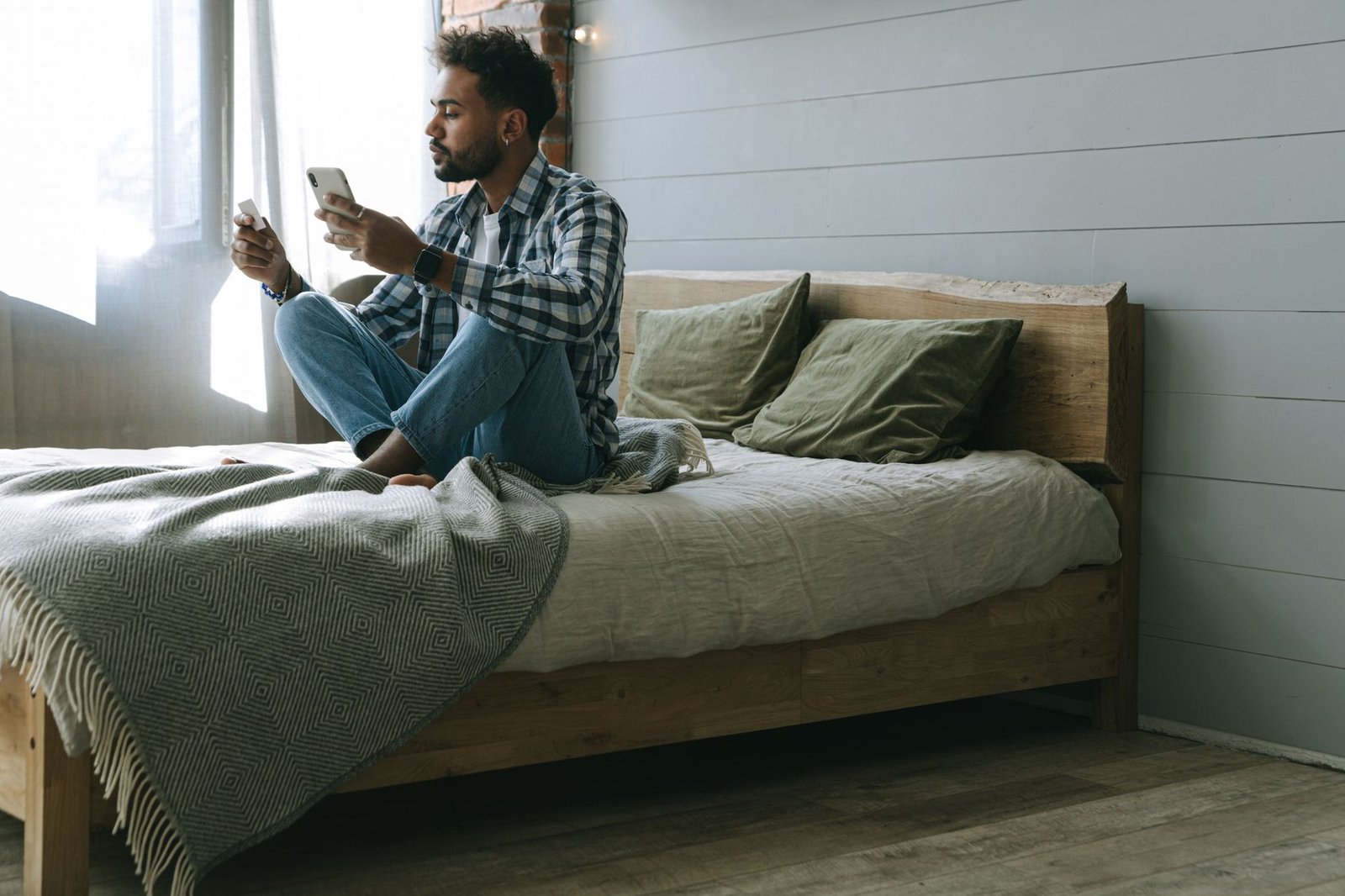 matras kopen — A man sits on a bed using a smartphone for online shopping and payments.